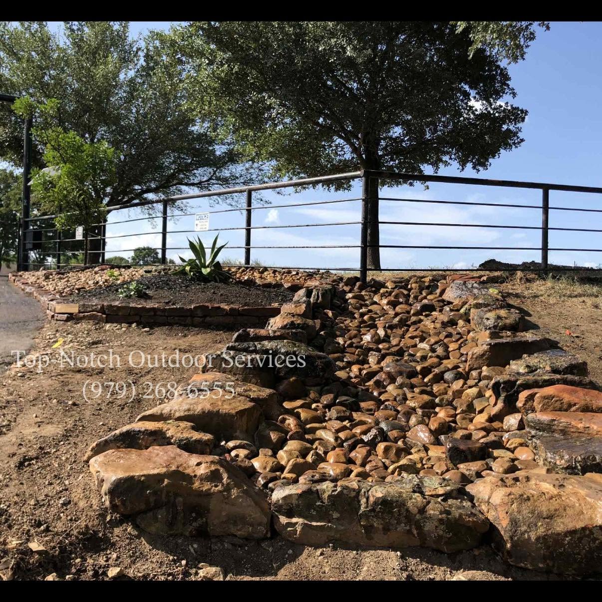 River-rock dry-creek drainage bed with stacked-stone border