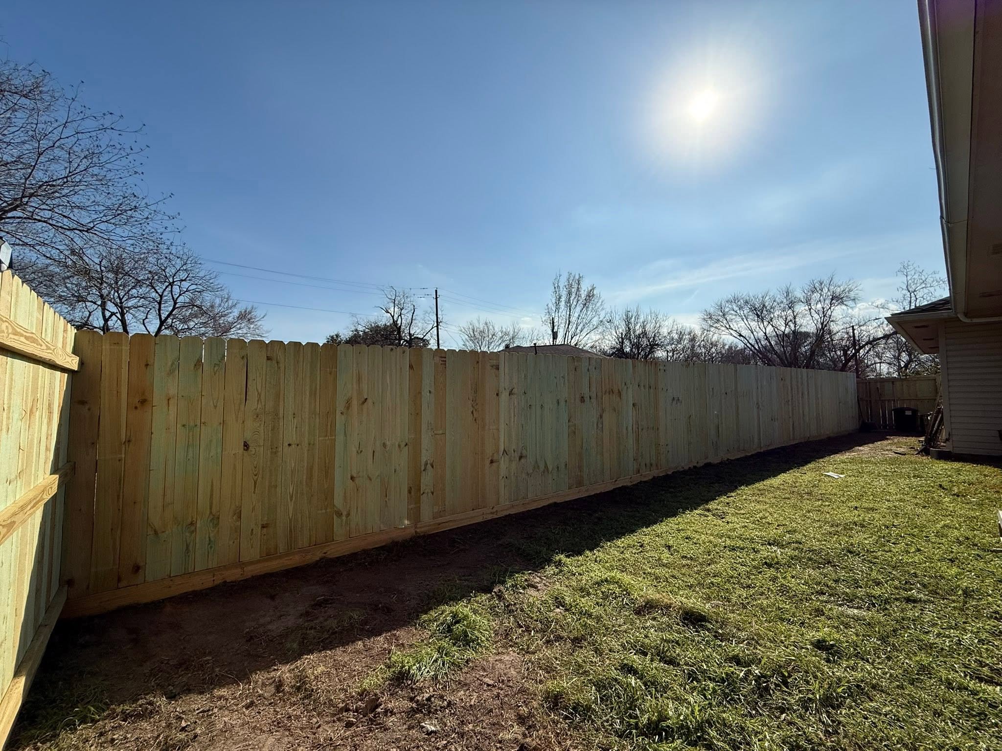 New dog-ear wood privacy fence beside a bright green lawn